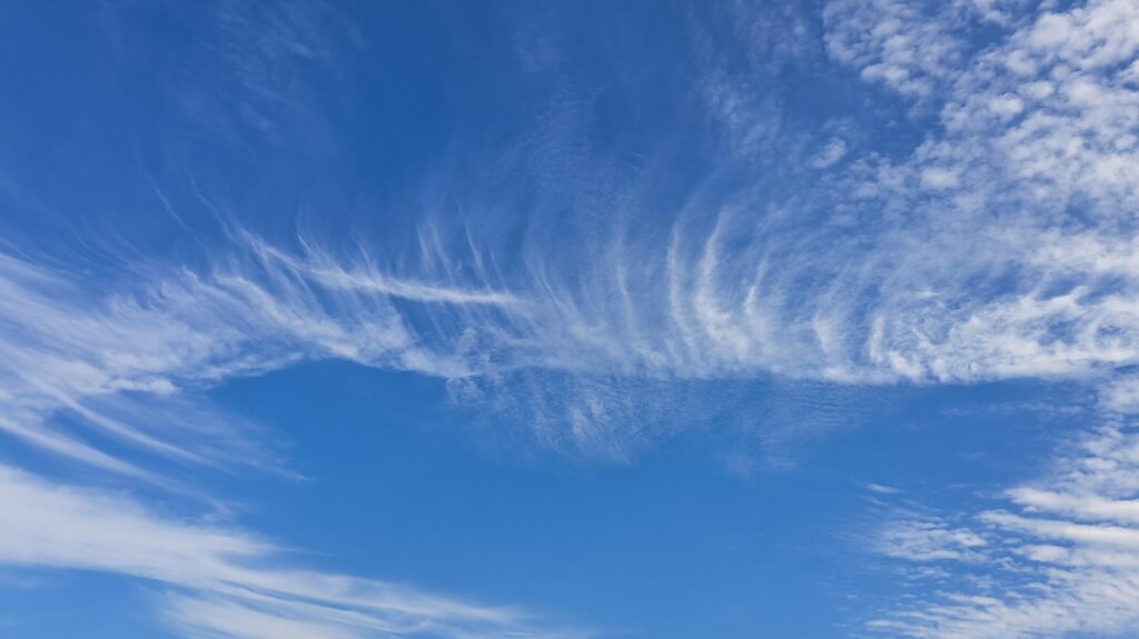Zarte weiße Wolken ziehen über einen strahlend blauen Himmel, ihre sanften Formen spiegeln die Ruhe wider, die man während der Trauerbegleitung beim Abschied nehmen sucht. Die friedliche Szene suggeriert ein Gefühl von Komfort und schönem Wetter.