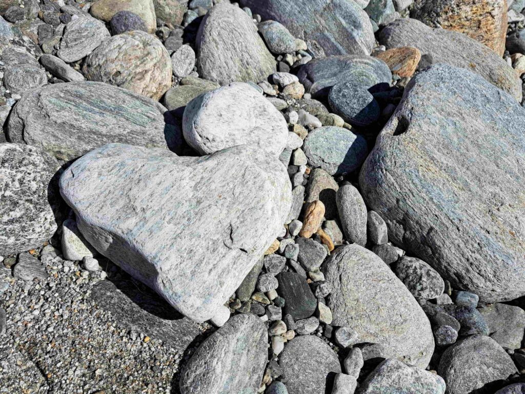 Eine Gruppe grauer Felsen und Kieselsteine unterschiedlicher Größe auf dem Boden, mit einem markanten Felsen im Vordergrund, der die Form eines Herzens hat - eine stimmungsvolle Szene, die den Abschied inmitten der ruhigen Landschaft der Ostschweiz symbolisiert.