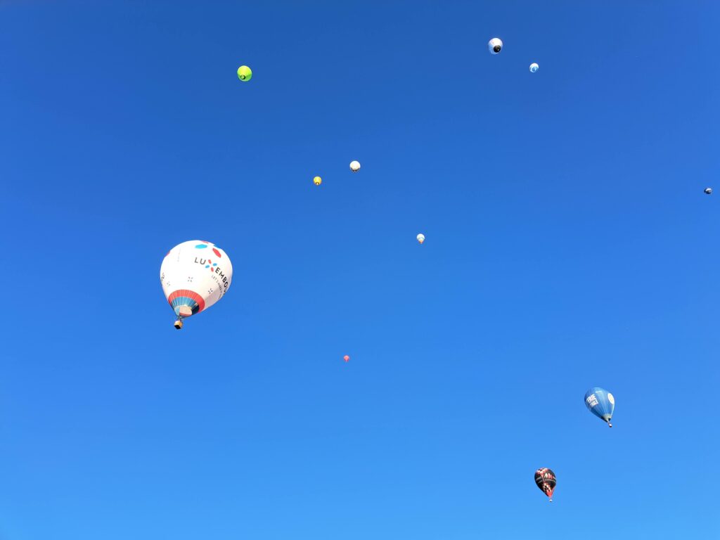 Mehrere farbenfrohe Heissluftballone schweben in unterschiedlichen Höhen und Abständen am klaren blauen Himmel über der Ostschweiz.